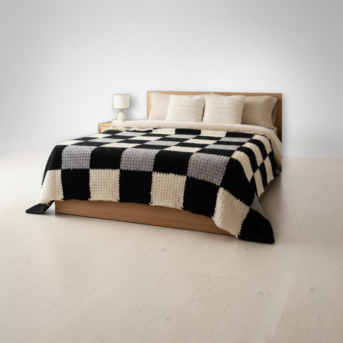 Chunky knit blanket in an oversized black, grey and cream checkerboard, spread across a wooden bed.