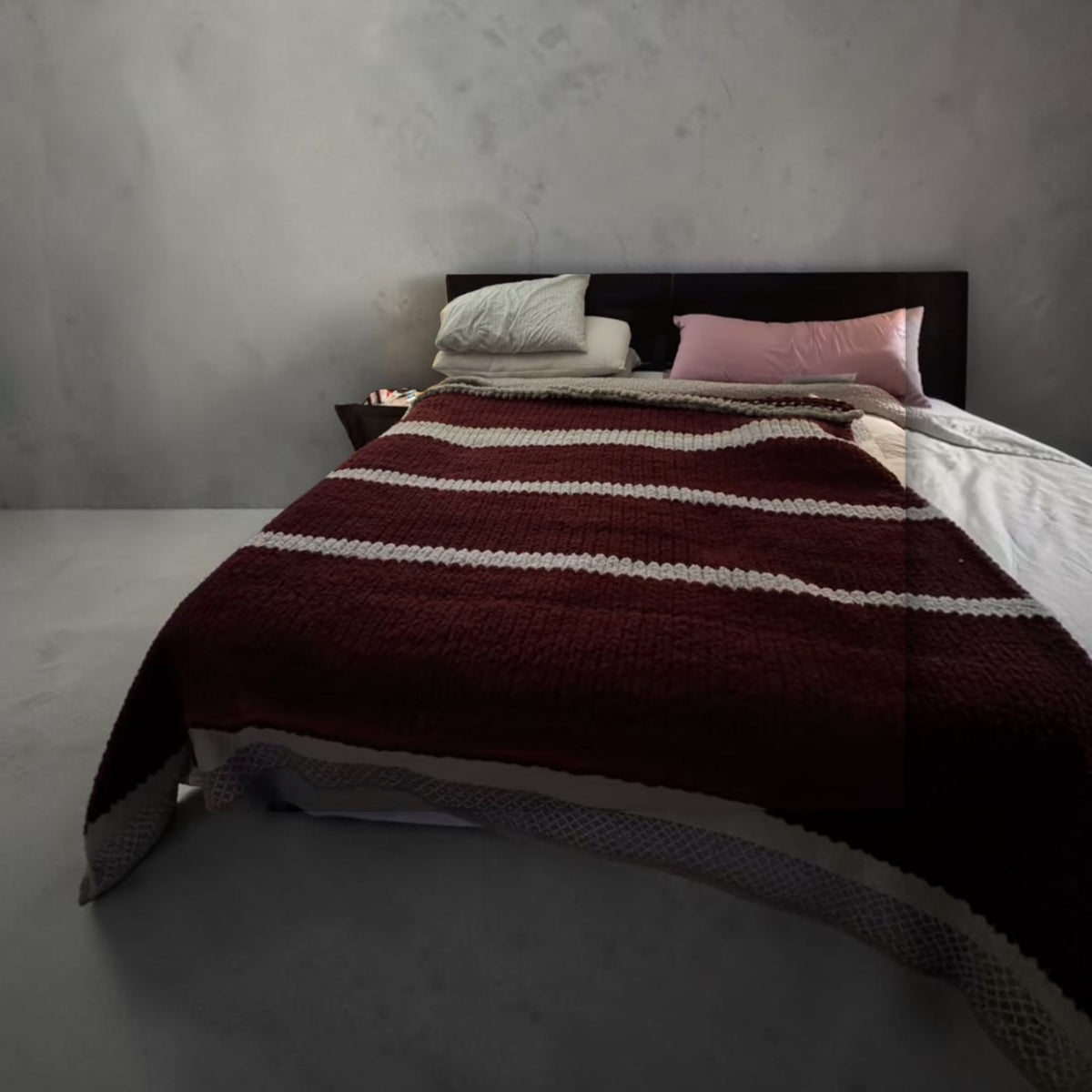 Chunky knit blanket in deep burgundy with cream horizontal stripes, draped across a bed.