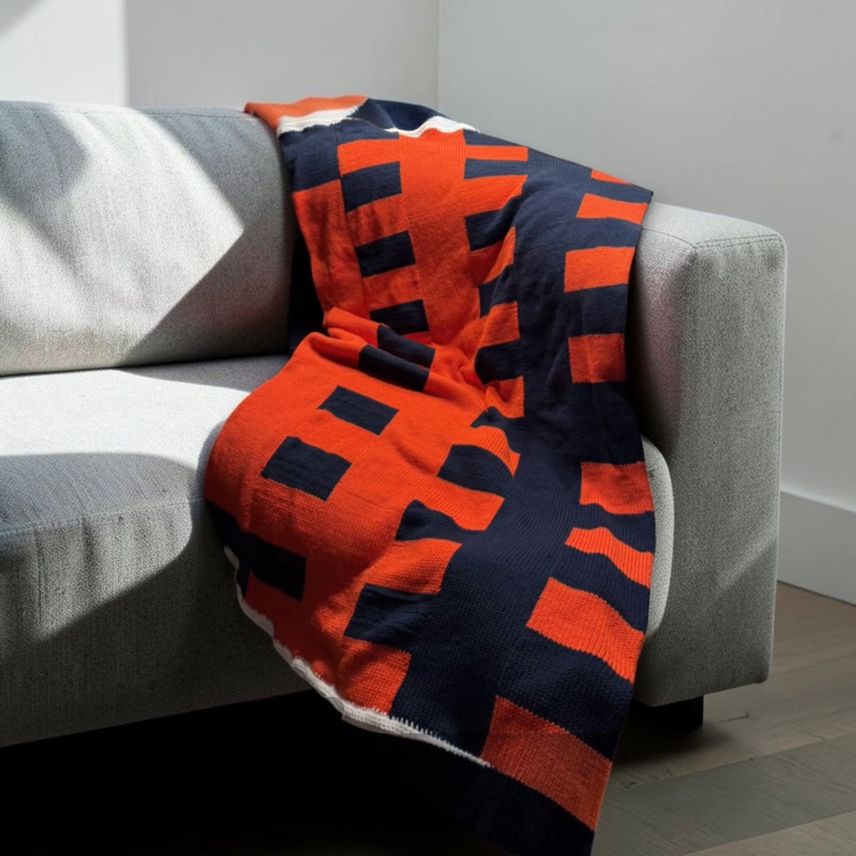Knit throw in a bold orange and navy interlocking colorblock pattern, draped over a grey sofa.