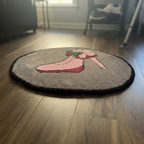 Oval hand-tufted rug with a retro pin-up illustration in pink, red and green on a grey background.