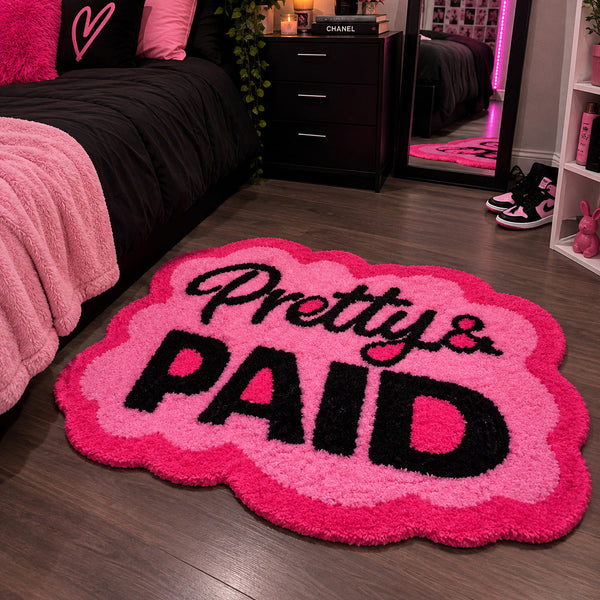 Cloud-shaped hand-tufted rug in hot pink with black "Pretty & Paid" lettering and a scalloped edge.